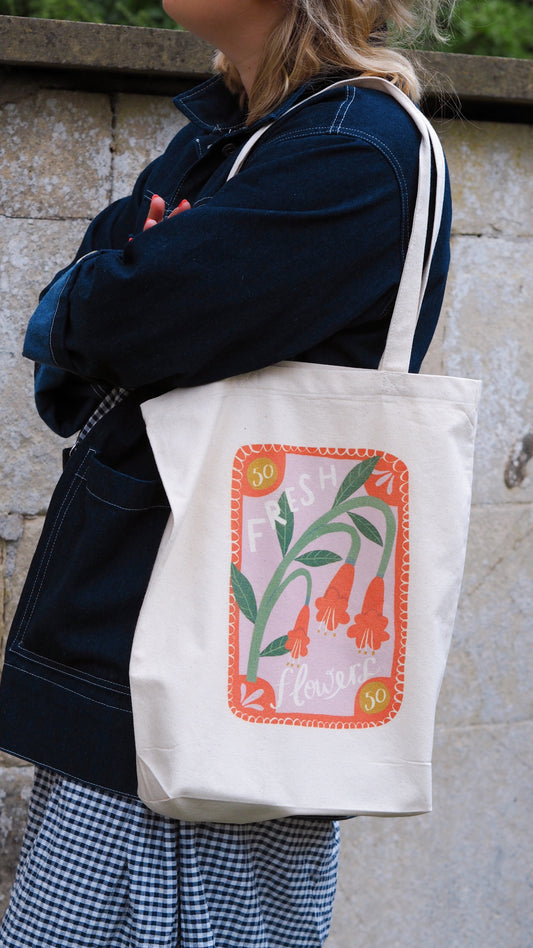 tote bag with red, lilac and green floral print. stamp design that says 'fresh flowers' 