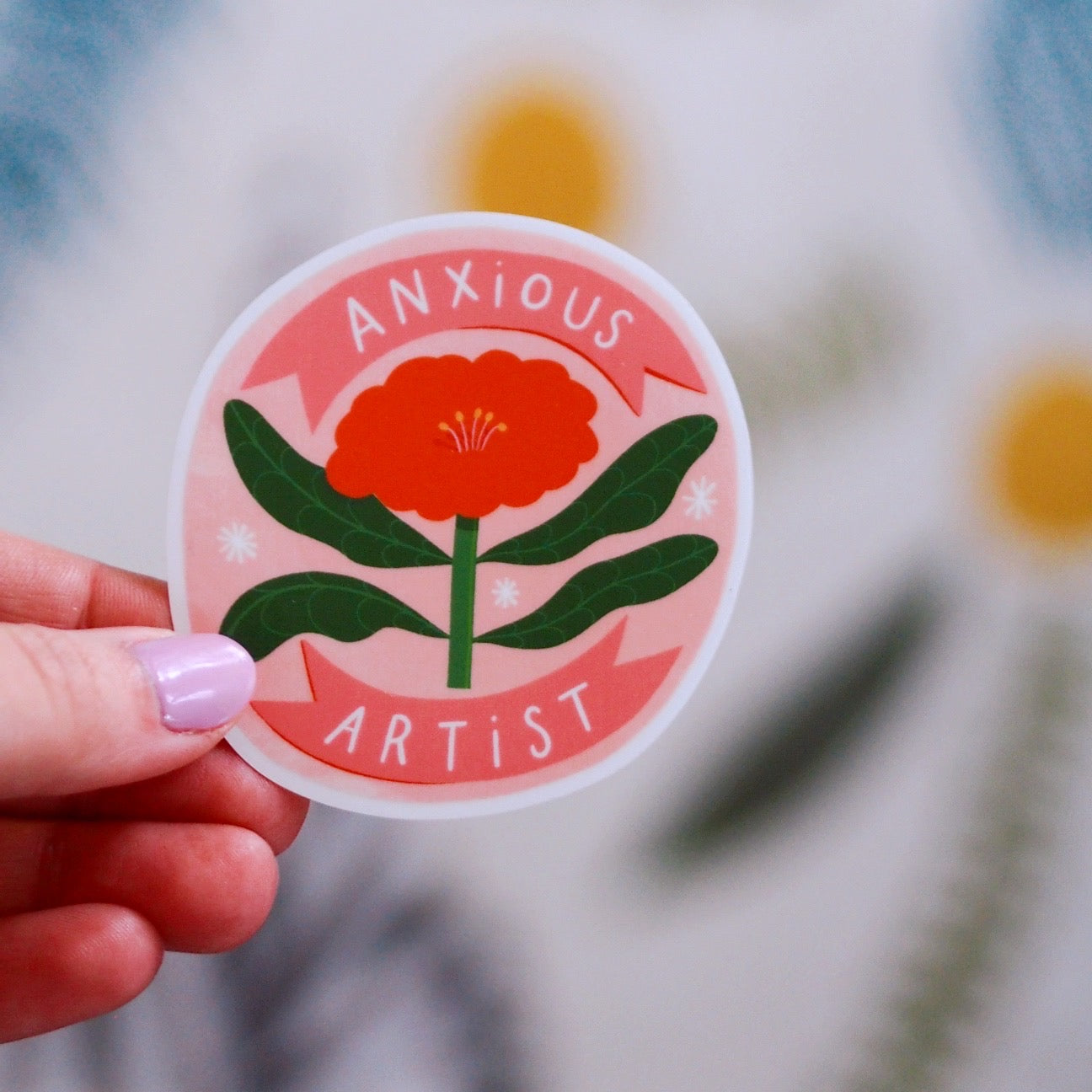 round vinyl sticker with a big red flower on it, the text reads 'anxious artist' background is pink and leaves are green