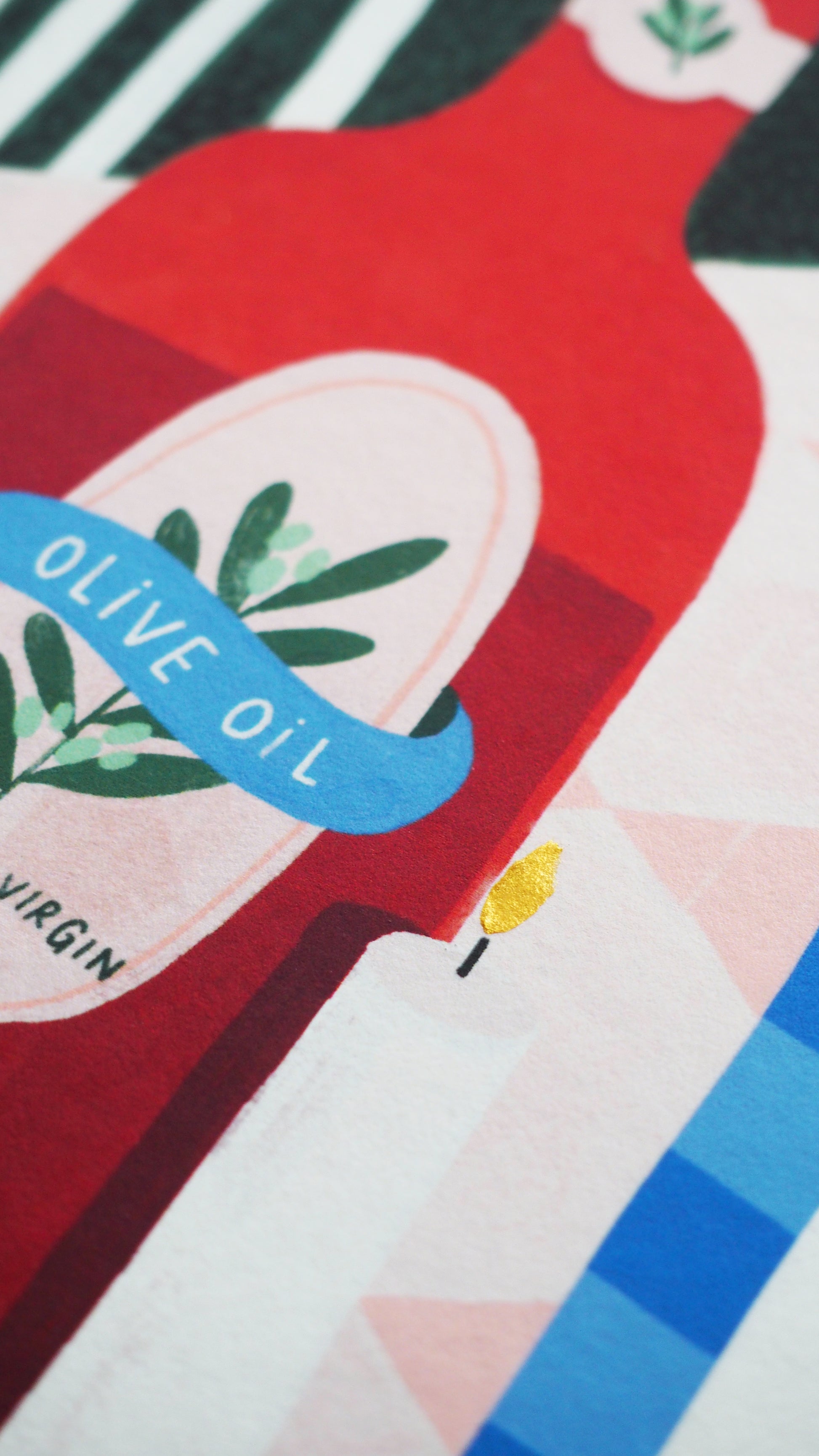 limited edition print, of a Mediterranean table, a plate of fish, bowl of olives, some oranges a candle and a bottle of olive oil on a gingham tablecloth. Green blue and terracotta colours. close up of the details on the print. finished with gold paint