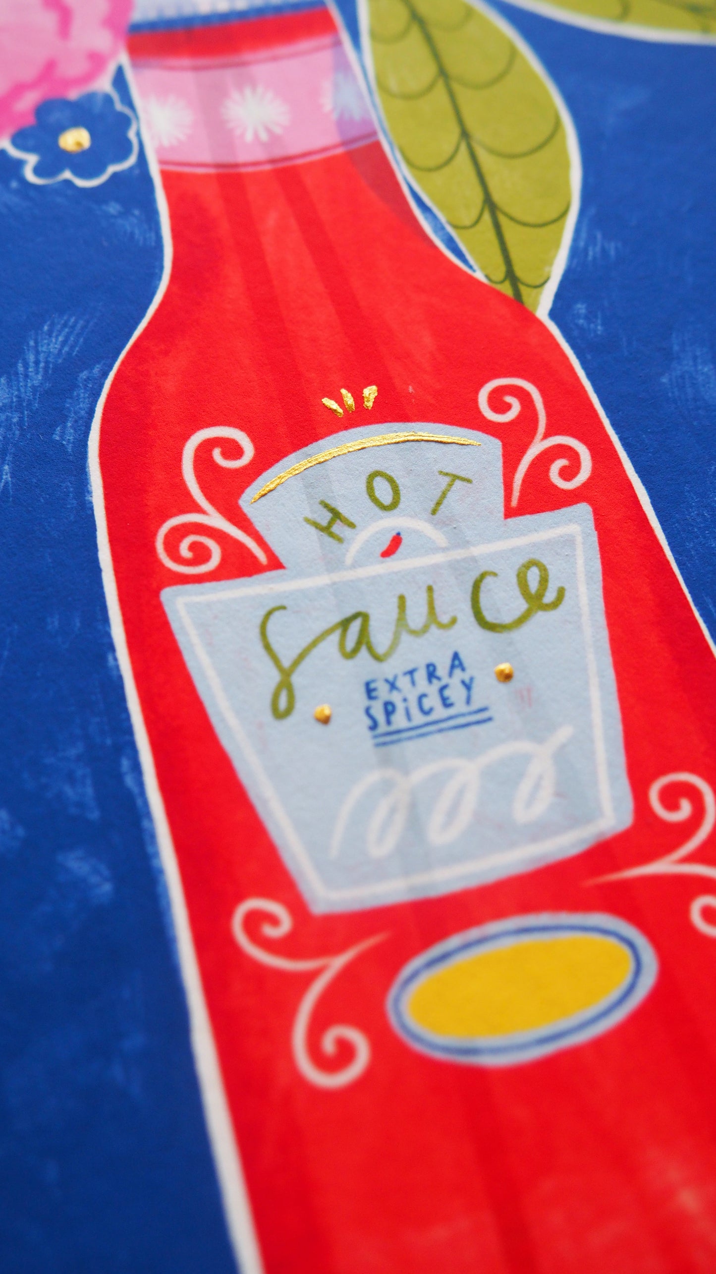 image of hot sauce, with pink flowers coming out of the top. the background is a royal blue and the patterned border is green and peach with stripes. showing gold details