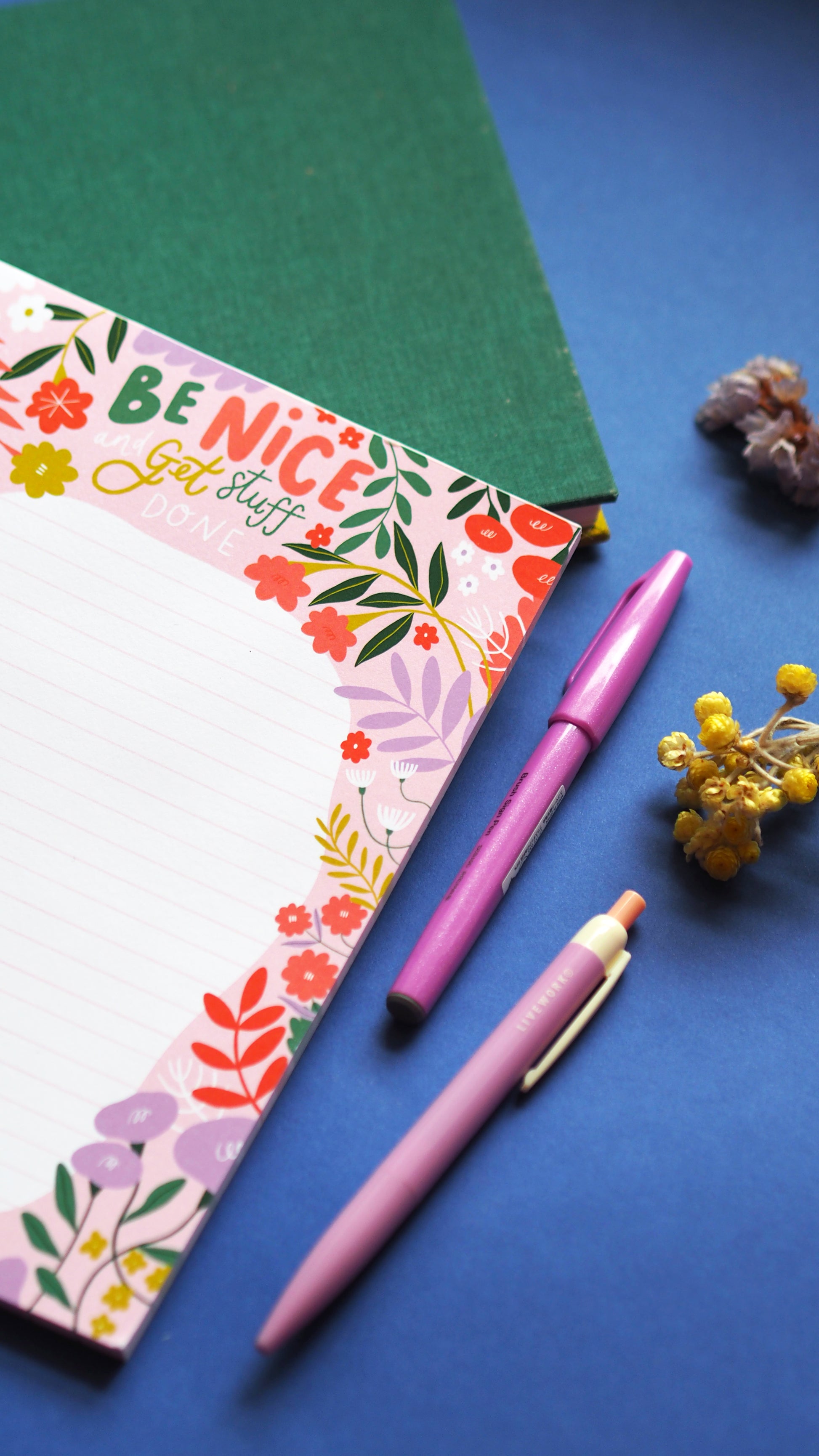 A5 list pad with 'be nice and get stuff done' written at the top in illustrated type, a floral border around the edge of the lined section with lots of fun florals and leaves. pink, green red and lilac are the main colours