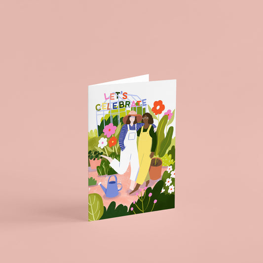 A6 greetings card of two girls with their arms around each other in a garden full of flowers and a greenhouse, text reads 'let's celebrate' in rainbow colours!