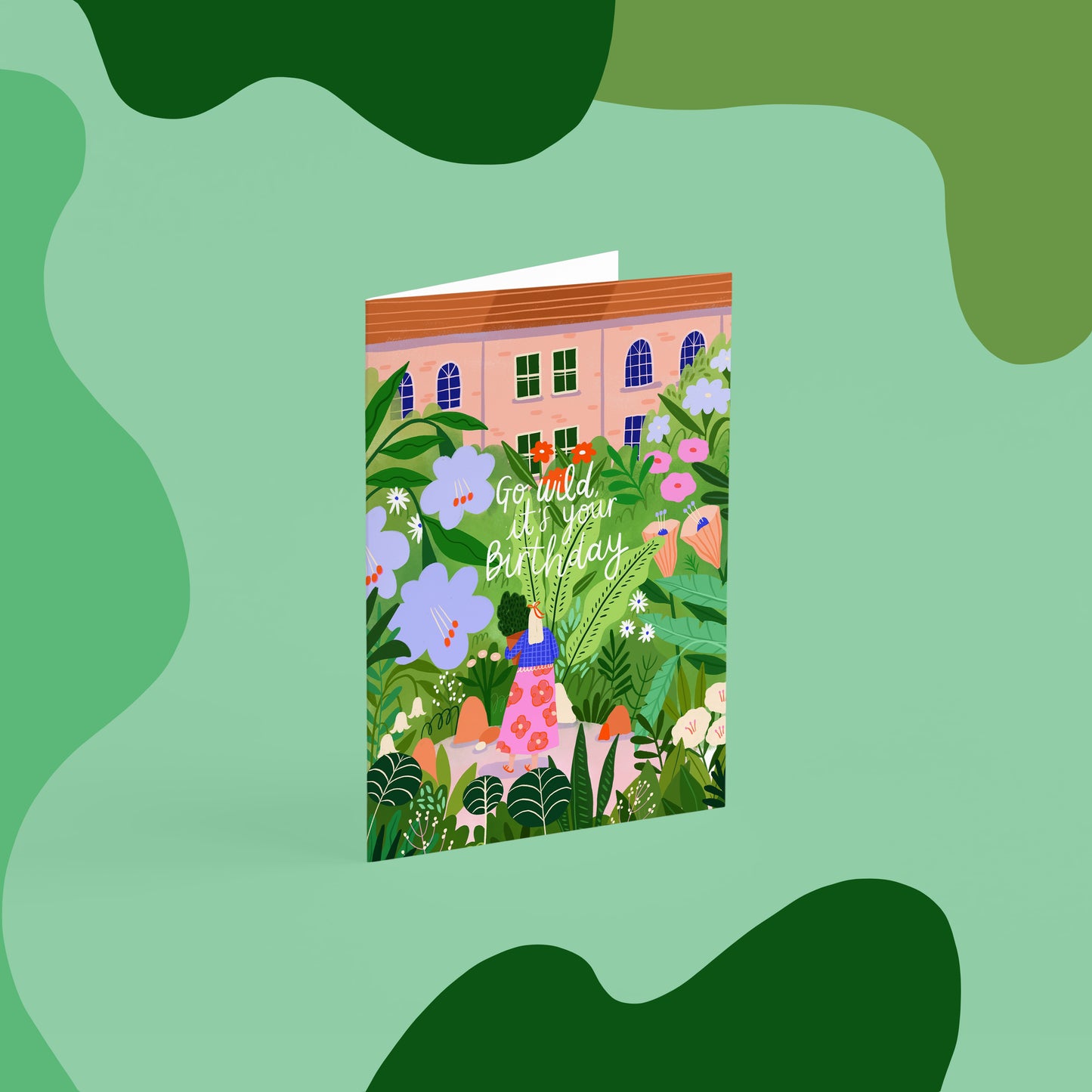 birthday card that reads ' go wild, it's your birthday'. the image is of a lady walking through a blooming garden with big flowers and plants and townhouses in the background, she is carrying a pot plant