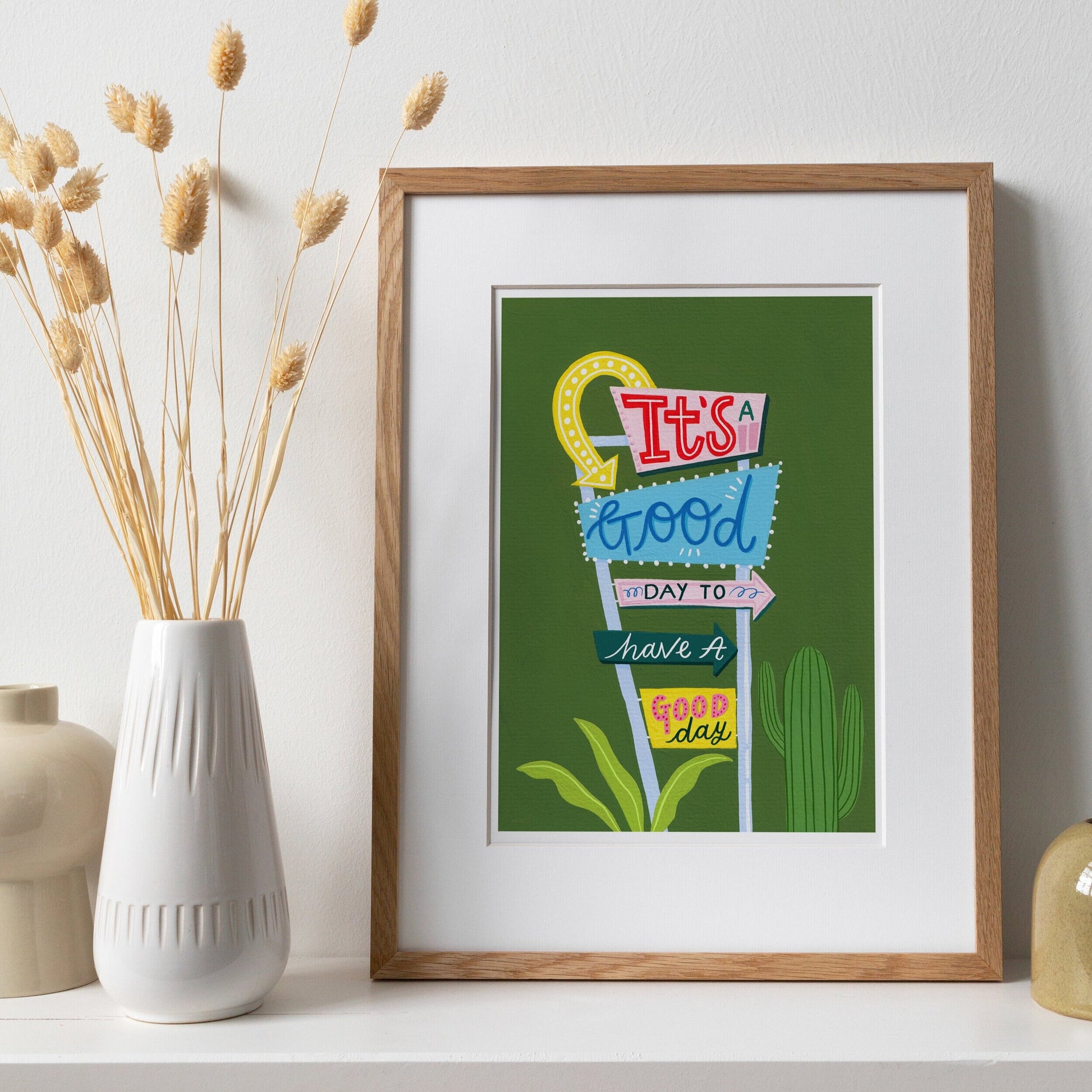 print of a retro motel sign, with green background and cacti, writing within the signs says 'it's a good day to have a good day'